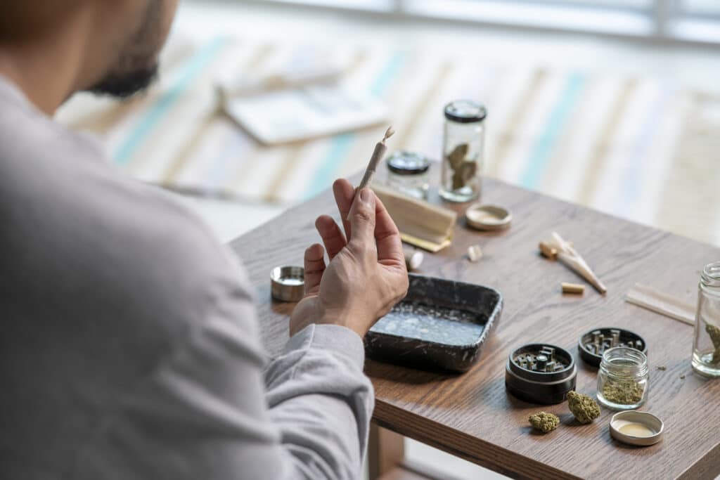 Young Asian man rolling a marijuana joint at home.